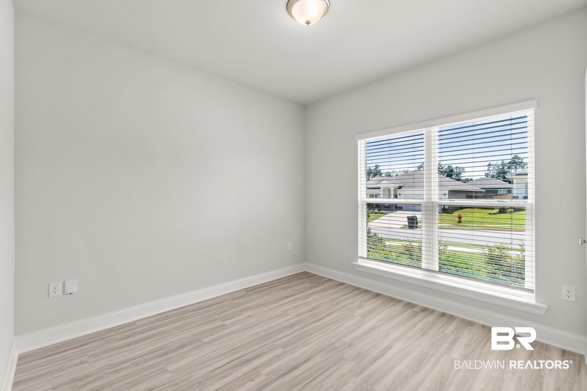 32125 Lyon Road Daphne, AL 36527 - Photo 25 of 70 Spacious room featuring light gray walls, wood-finish flooring, a large window with white blinds, and a flush-mount ceiling light fixture