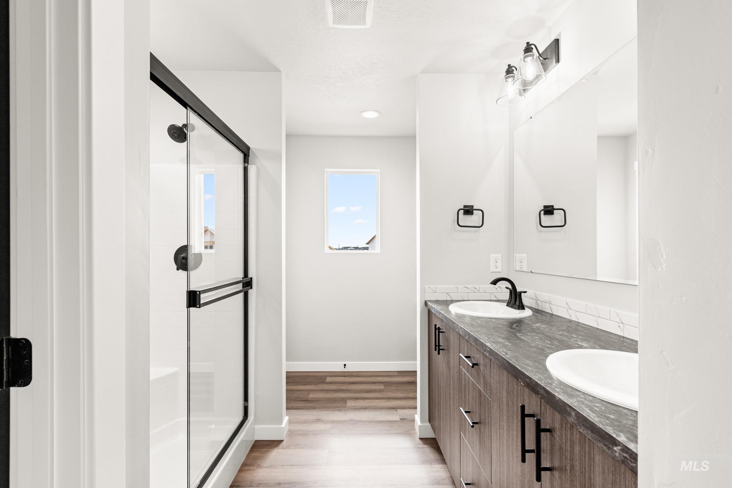 12830 Ropers Street Nampa, ID 83651 - Photo 12 of 18 Contemporary bathroom featuring a glass-enclosed shower with matte black fixtures, a double vanity with wood-finish cabinetry, dark countertops, and undermount sinks