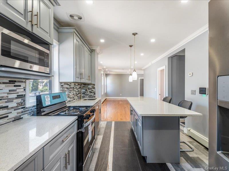176-27 Sunbury Road Queens, NY 11434 - Photo 16 of 31 Kitchen featuring gray cabinets, a breakfast bar, stainless steel appliances, hanging light fixtures, and light stone countertops