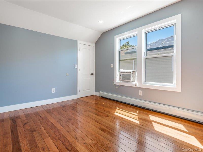 176-27 Sunbury Road Queens, NY 11434 - Photo 24 of 31 Spare room featuring a baseboard heating unit, lofted ceiling, hardwood / wood-style flooring, and cooling unit