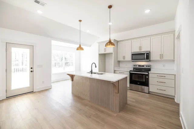 a kitchen with stainless steel appliances kitchen island granite countertop a sink a stove and a wooden floor