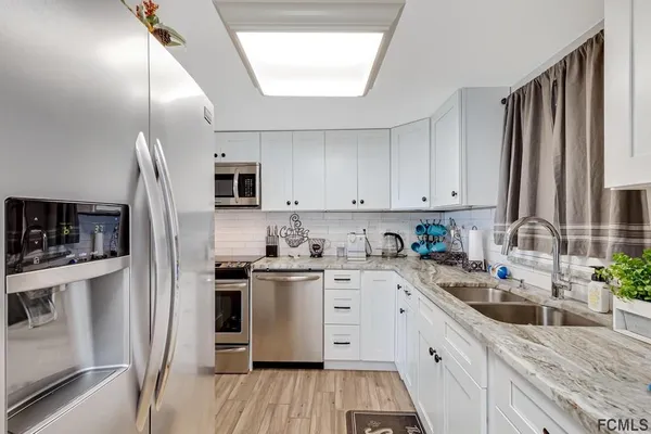 a kitchen with stainless steel appliances granite countertop a refrigerator a stove top oven a sink dishwasher and white cabinets with wooden floor