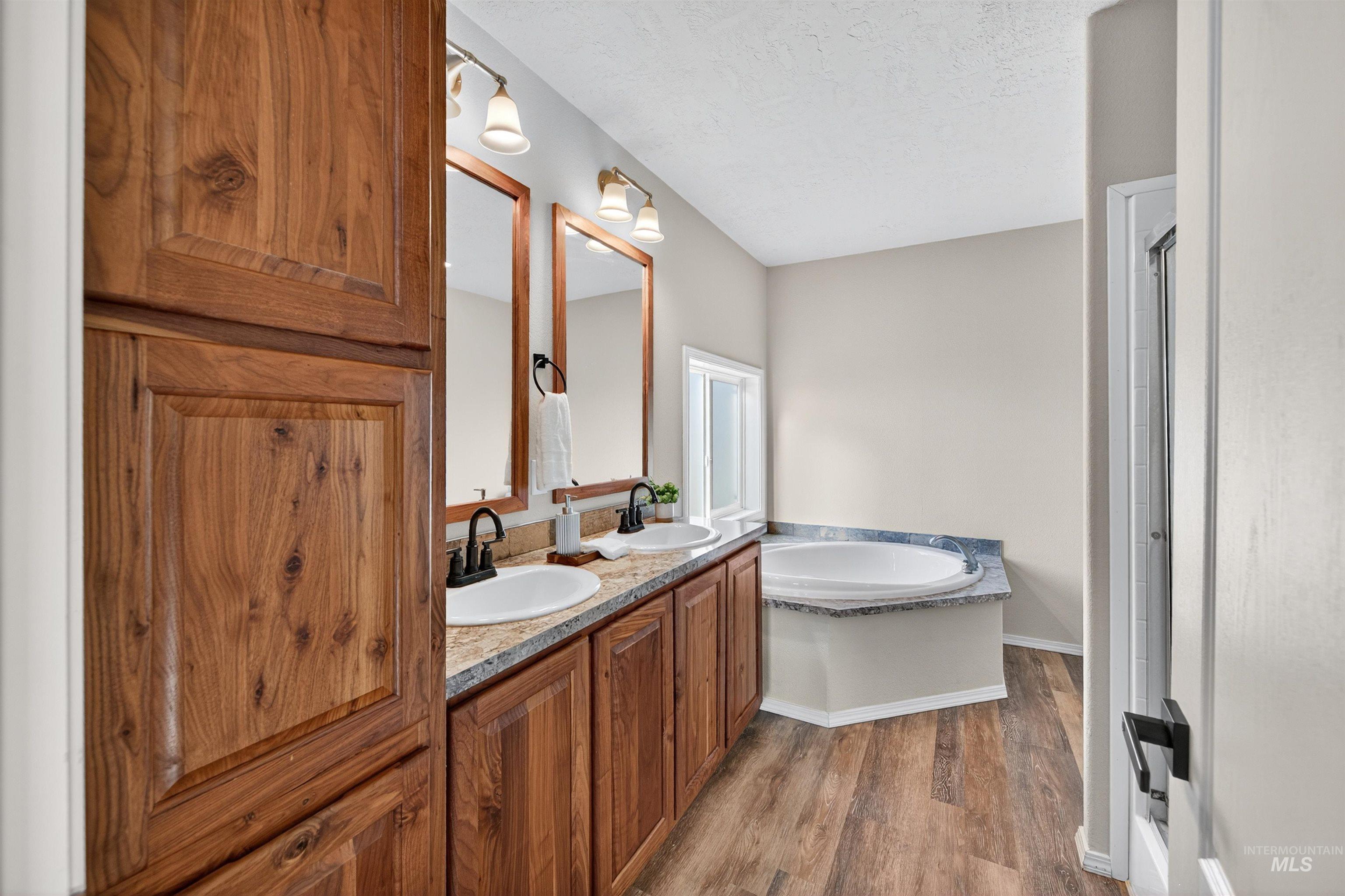 1203 Locker Avenue Parma, ID 83660 - Photo 24 of 49 Full bathroom with double vanity, a bath, dark wood finished floors, a textured ceiling, and a shower stall