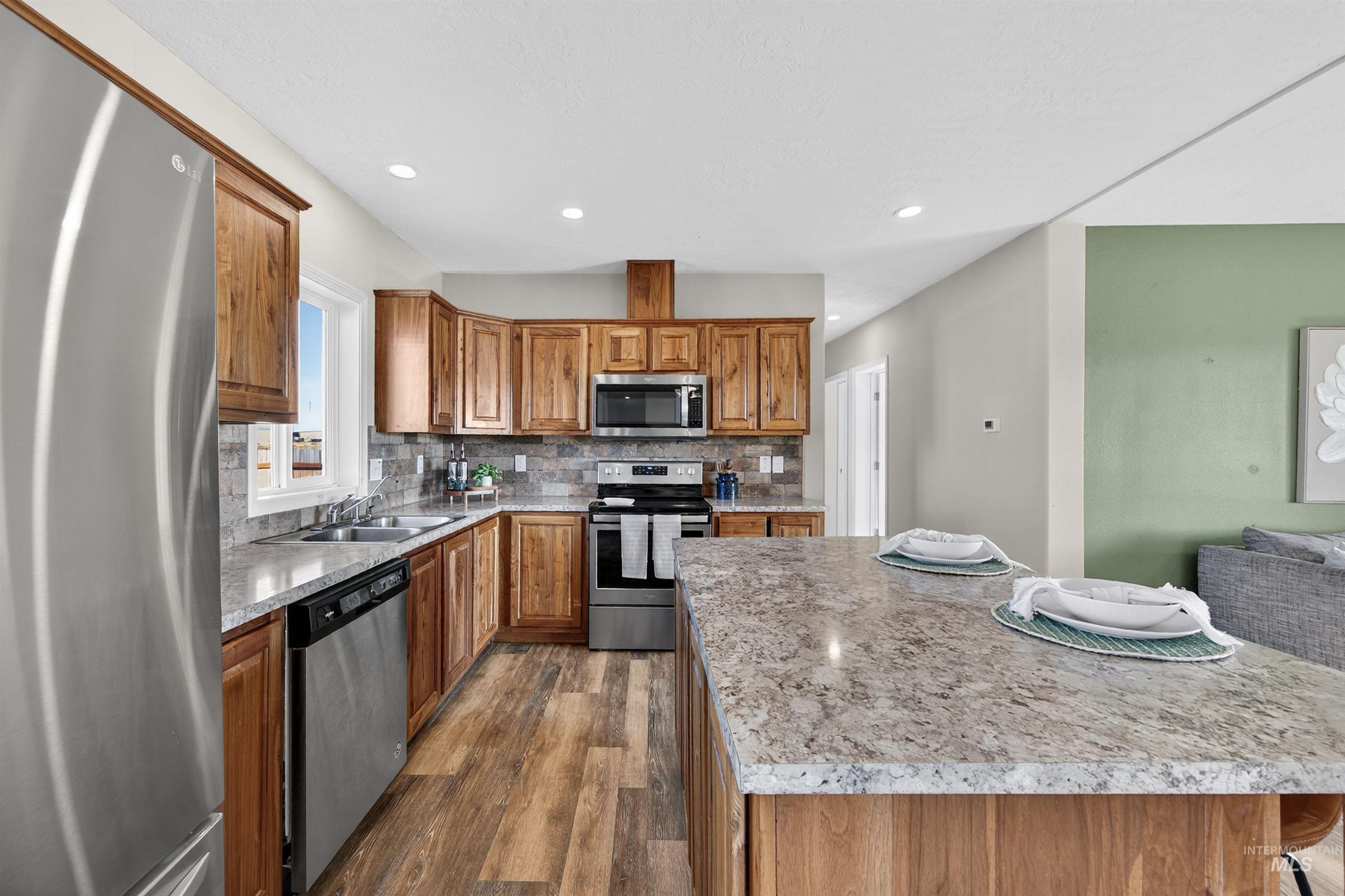 1203 Locker Avenue Parma, ID 83660 - Photo 7 of 49 Kitchen featuring appliances with stainless steel finishes, dark wood-style flooring, brown cabinets, backsplash, and a kitchen island