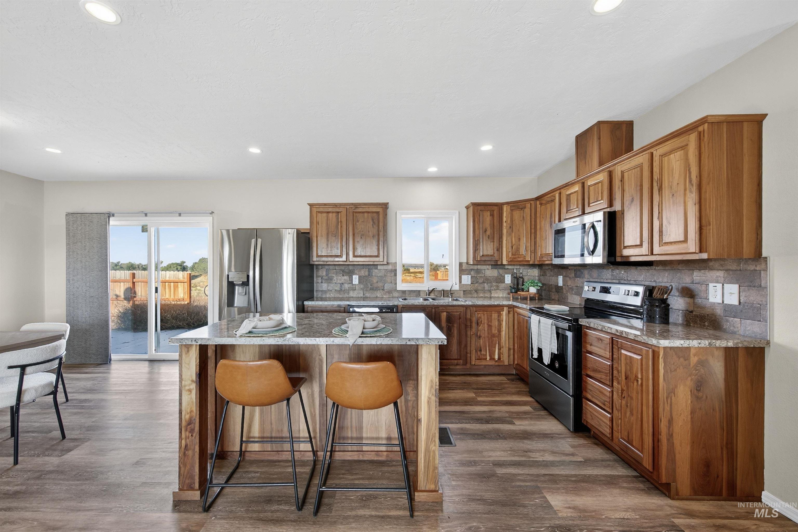 1203 Locker Avenue Parma, ID 83660 - Photo 7 of 49 Kitchen with stainless steel appliances, brown cabinetry, backsplash, a kitchen island, and a kitchen breakfast bar