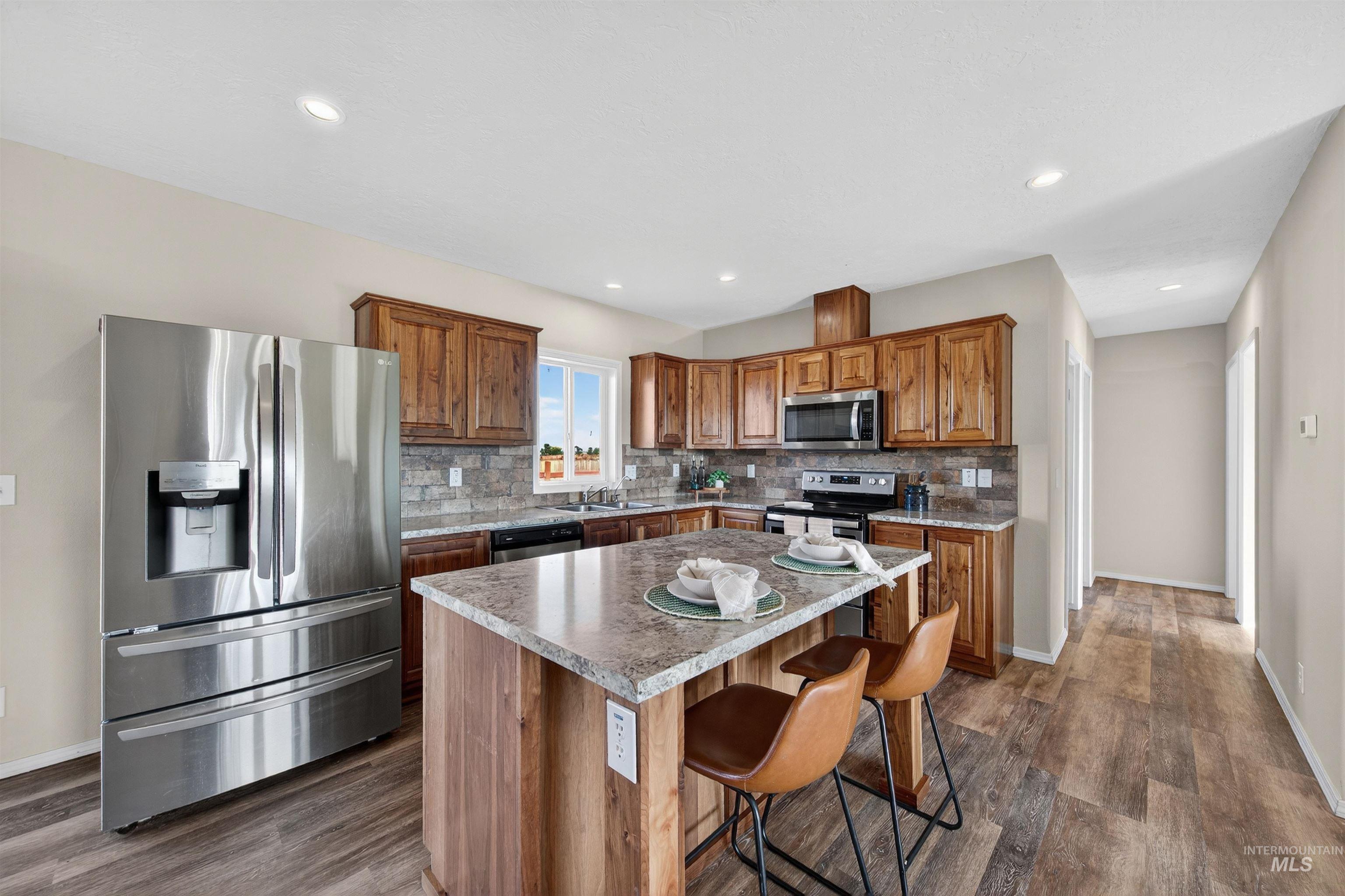 1203 Locker Avenue Parma, ID 83660 - Photo 9 of 49 Kitchen featuring stainless steel appliances, backsplash, brown cabinets, a center island, and a breakfast bar
