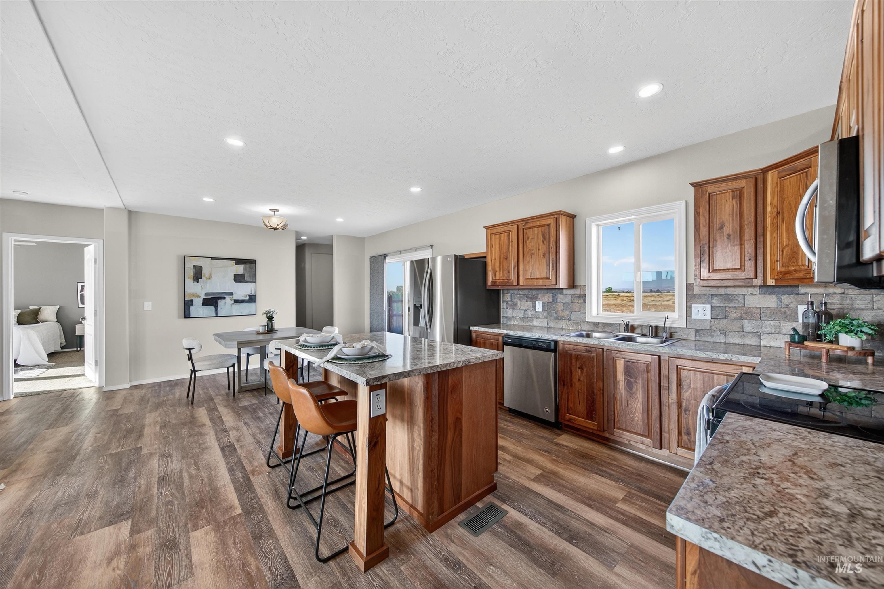 1203 Locker Avenue Parma, ID 83660 - Photo 10 of 49 Kitchen featuring brown cabinetry, a center island, decorative backsplash, a breakfast bar area, and stainless steel appliances