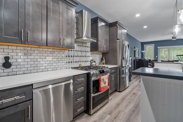 a kitchen with stainless steel appliances granite countertop a stove a sink dishwasher and a refrigerator with wooden cabinets