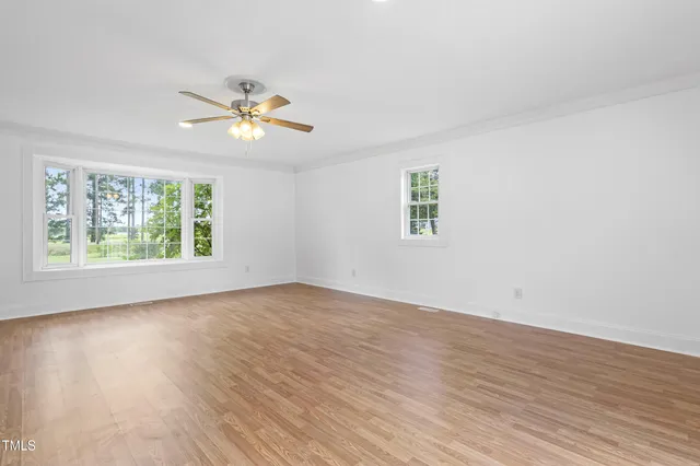 an empty room with wooden floor ceiling fan and windows