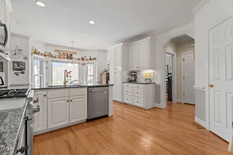 a kitchen with stainless steel appliances granite countertop white cabinets a sink a stove a refrigerator and microwave with wooden floor