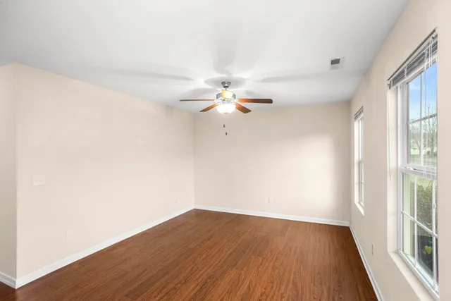 an empty room with wooden floor fan and windows