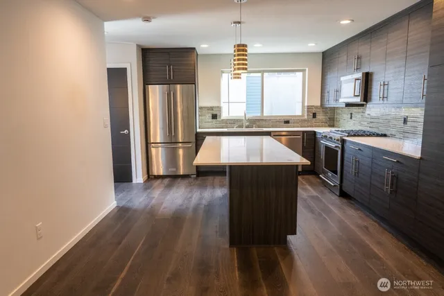 a kitchen with kitchen island granite countertop wooden floors stainless steel appliances a sink and a window