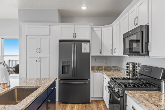 1343 North Trapper Loop Garden City, UT 84028 - Photo 25 of 56 Dual tone kitchen with black appliances, light stone countertops, dual tone cabinets, and light wood-style flooring