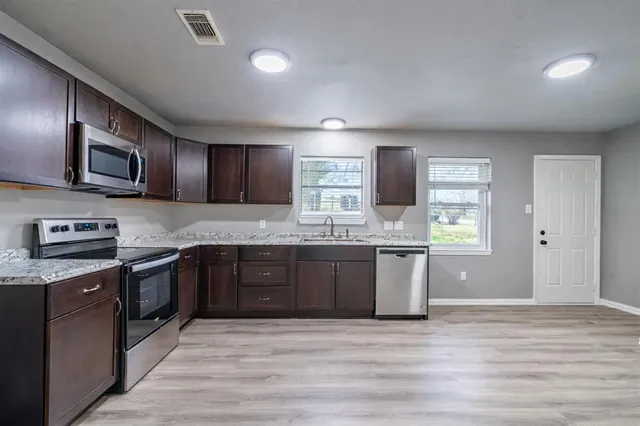 a large kitchen with stainless steel appliances granite countertop a stove a sink dishwasher a microwave oven and a refrigerator with wooden floor