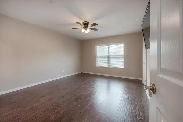 an empty room with wooden floor chandelier fan and windows
