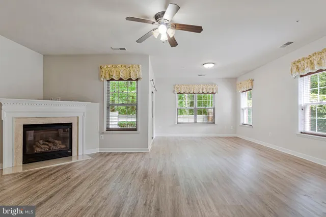 a view of an empty room with wooden floor fireplace and a window