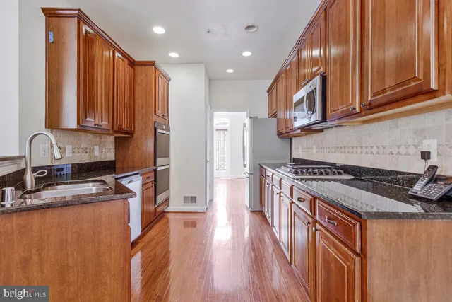 a kitchen with stainless steel appliances granite countertop a stove a sink dishwasher and a refrigerator with wooden floor