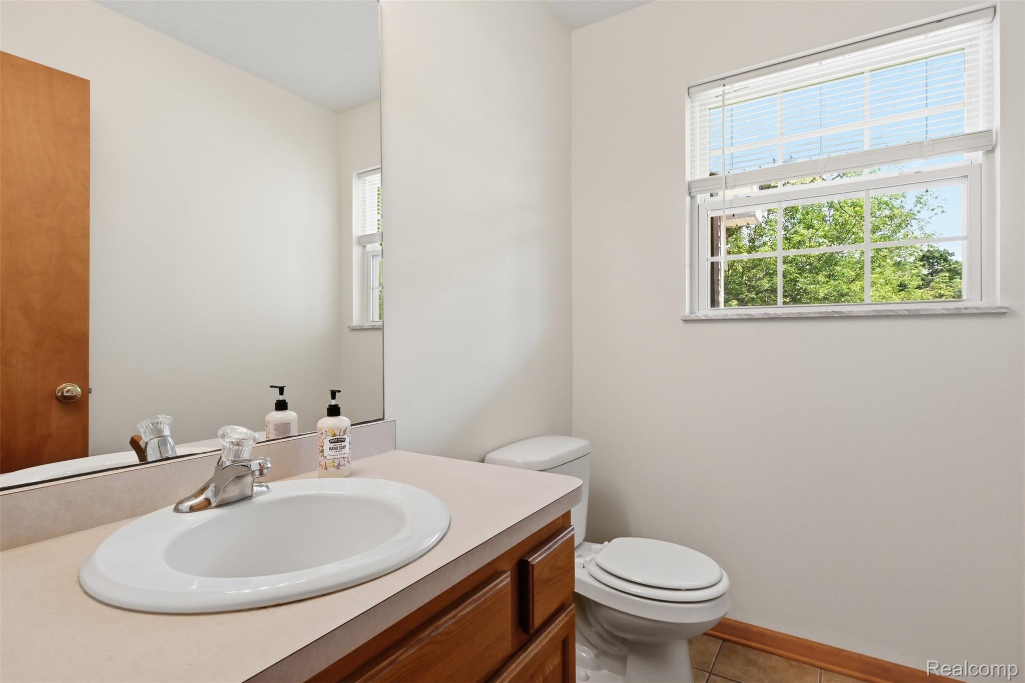 4482 Pleasant Valley Road Brighton, MI 48114 - Photo 13 of 35 Bathroom featuring a wood-finish vanity with an integrated sink, a large wall-mounted mirror, and a window with horizontal blinds