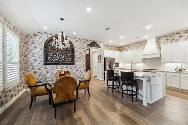 a kitchen with stainless steel appliances granite countertop a stove a sink a dining table and chairs with wooden floor