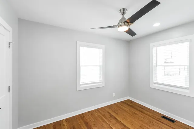 an empty room with wooden floor ceiling fan and windows