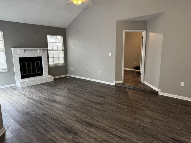 an empty room with wooden floor fireplace and windows