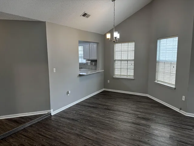 an empty room with wooden floor chandelier and windows
