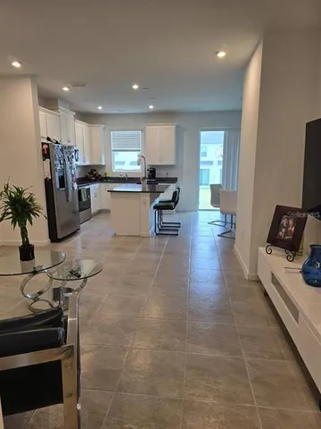 a living room with stainless steel appliances furniture a rug and a kitchen