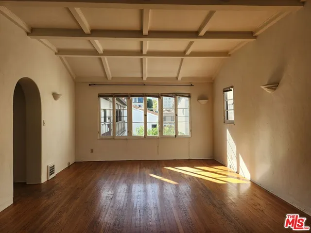 an empty room with wooden floor and windows with curtains