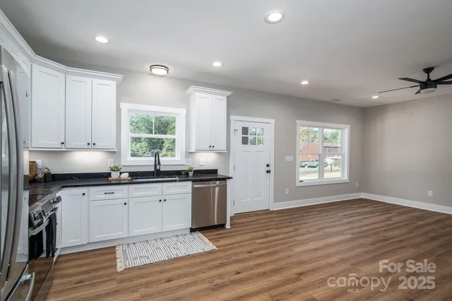 a kitchen with stainless steel appliances granite countertop a stove a sink and white cabinets with wooden floor