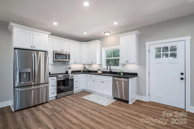 a kitchen with granite countertop a refrigerator stove a sink and dishwasher with wooden floor