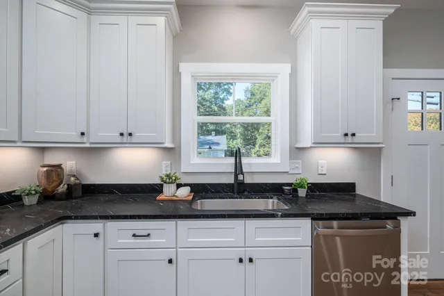 a kitchen with granite countertop white cabinets white appliances and a wide window