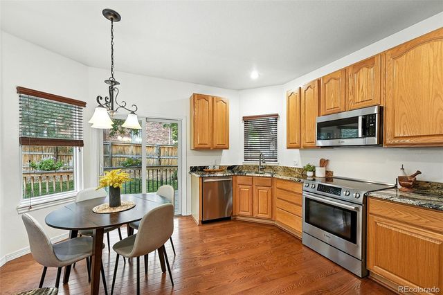 a kitchen with stainless steel appliances granite countertop a stove top oven a sink dishwasher a dining table and chairs with wooden floor