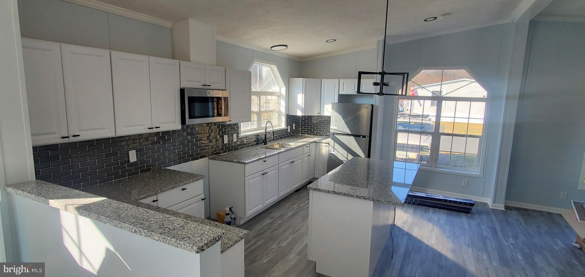 a kitchen with granite countertop a refrigerator a stove a microwave and island with wooden floor