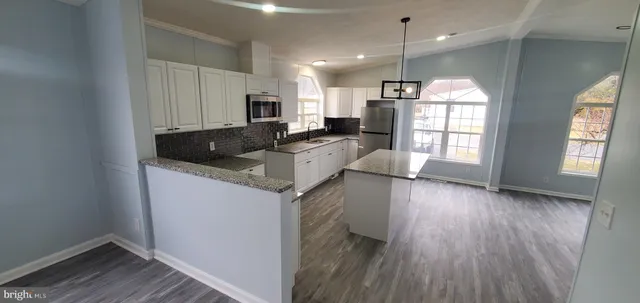 a kitchen with stainless steel appliances granite countertop a refrigerator a sink dishwasher a stove and white countertops with wooden floor