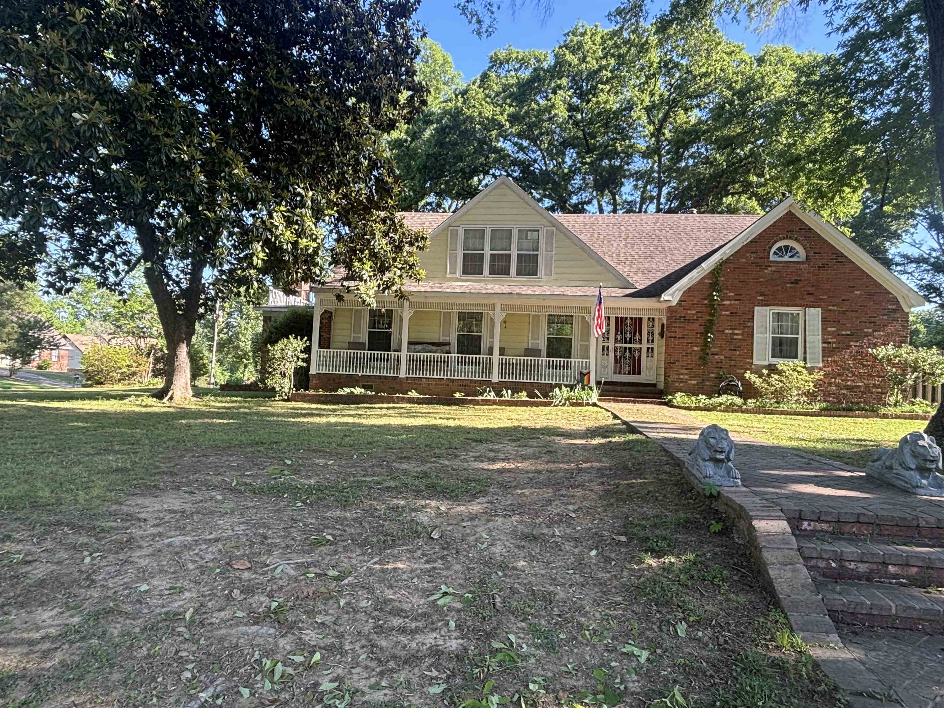 Brick and siding exterior featuring a covered front porch with white railings, a front entrance with a screen door, and a brick pathway with tiered steps