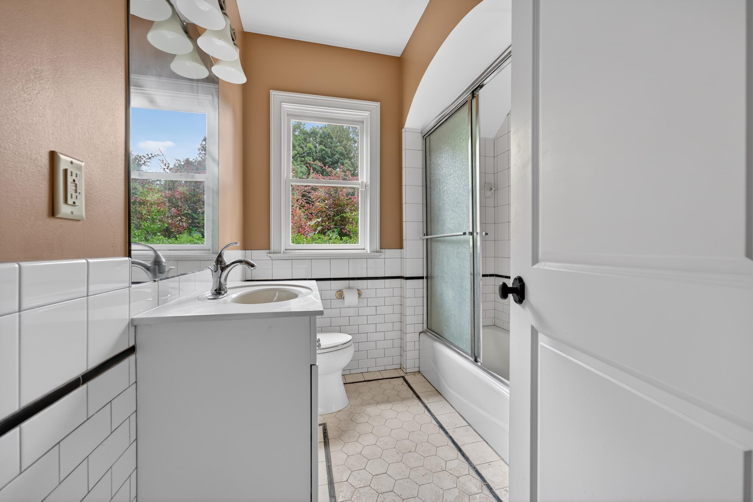 530 West Raines Road Memphis, TN 38109 - Photo 26 of 38 Bathroom featuring a single vanity with chrome faucet, white subway tile surround, hexagonal floor tile, and a tub with sliding glass doors