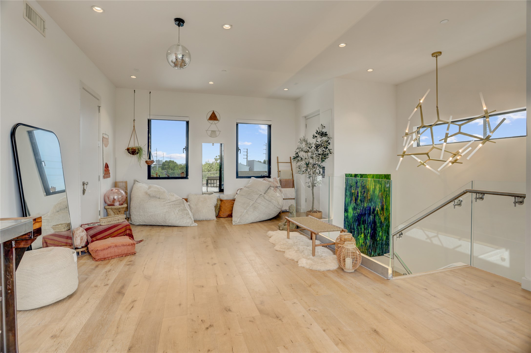 1807 Indiana Street Houston, TX 77006 - Photo 28 of 35 Fourth-Floor Lounge Alternate: Reverse view of the top-floor flex space, highlighting the glass-enclosed floating staircase, wide-plank wood flooring, recessed lighting, and bright square windows showcasing neighborhood views.