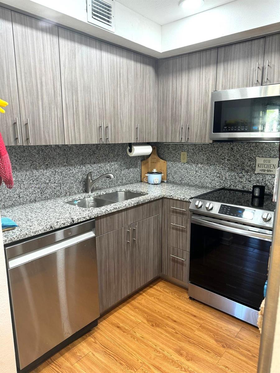 9030 Southwest 125th Avenue, Unit E210 Miami, FL 33186 - Photo 12 of 18 a kitchen with granite countertop wood cabinets stainless steel appliances and a sink