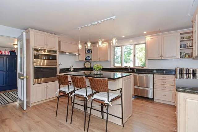 a kitchen with stainless steel appliances granite countertop a stove top oven a sink a refrigerator and white cabinets with wooden floor