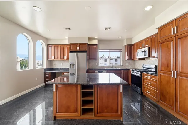 a kitchen with stainless steel appliances granite countertop a refrigerator a stove a sink dishwasher and wooden cabinets with wooden floor