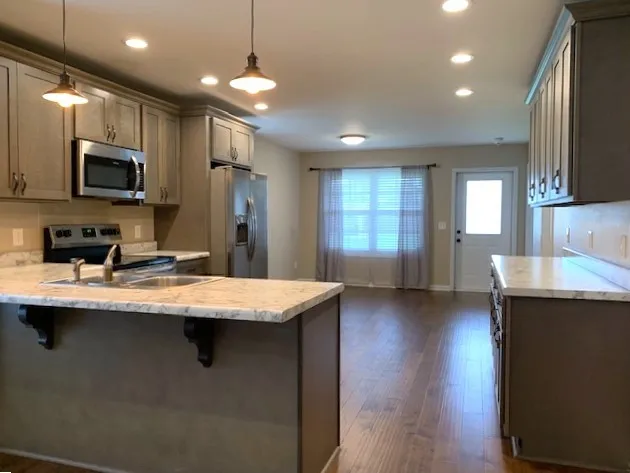 a kitchen with stainless steel appliances granite countertop a sink a stove top oven a refrigerator with wooden floors and a fireplace