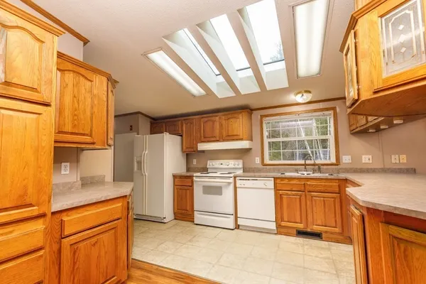 a kitchen with stainless steel appliances granite countertop a refrigerator a sink dishwasher a stove and white countertops with wooden floor