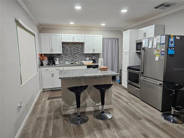 a kitchen with stainless steel appliances granite countertop a refrigerator a stove a sink dishwasher and white cabinets with wooden floor