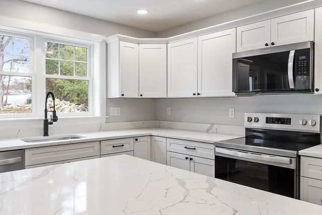 a kitchen with stainless steel appliances granite countertop a stove a sink a refrigerator and white cabinets