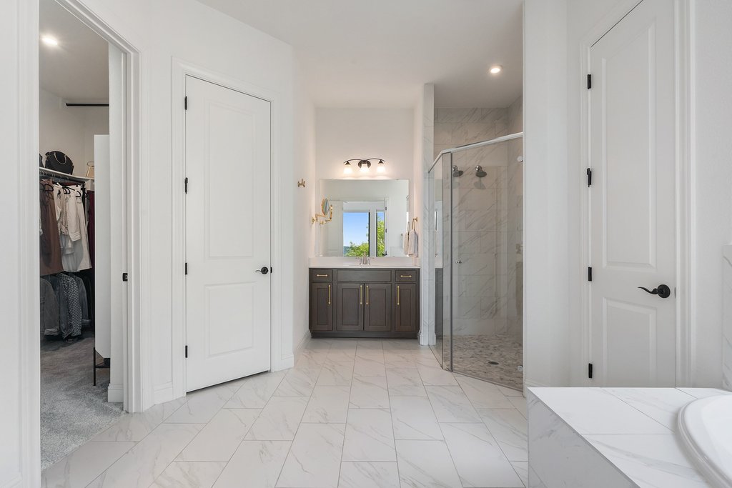 1221 Siena Sunset Road Leander, TX 78641 - Photo 23 of 39 Expansive bathroom featuring large format tile flooring, a dark wood-finish vanity with a single sink, a frameless glass shower enclosure with tile surround, and a separate water closet