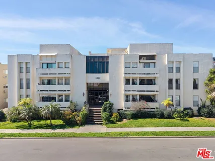 a front view of a residential apartment building with a yard and large trees