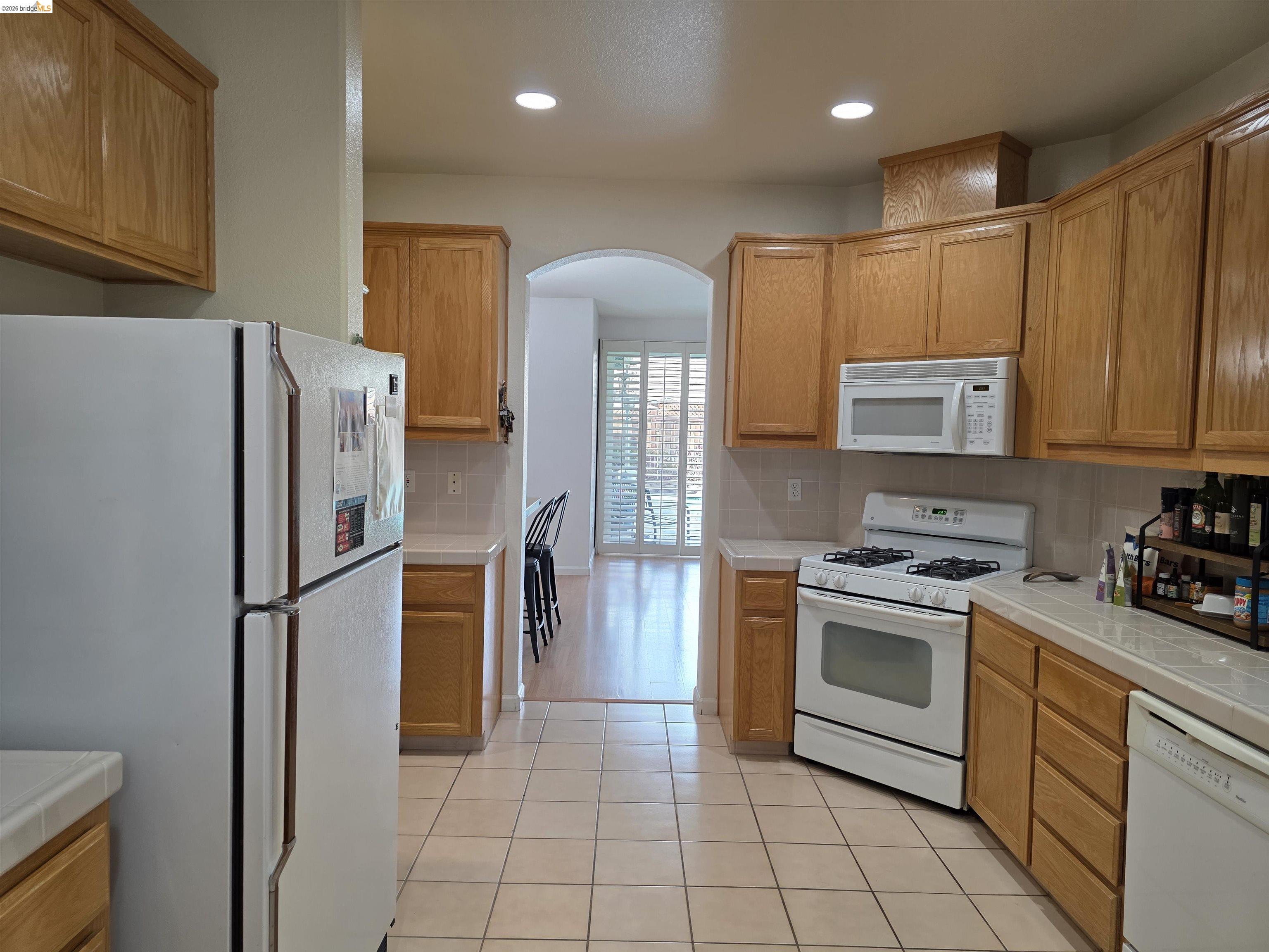 2607 Glow Road Riverbank, CA 95367 - Photo 23 of 42 Kitchen featuring light wood cabinetry, white appliances, tiled flooring, and an arched doorway