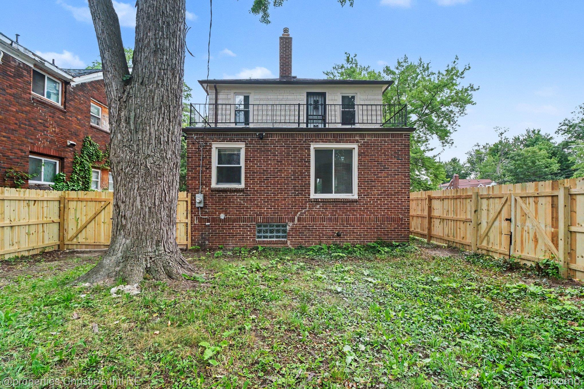 5911 Yorkshire Road Detroit, MI 48224 - Photo 13 of 14 Rear brick exterior featuring a balcony with metal railing, white window trim, and a prominent chimney