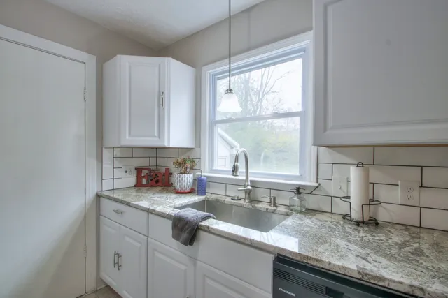 a kitchen with granite countertop a sink window and cabinets