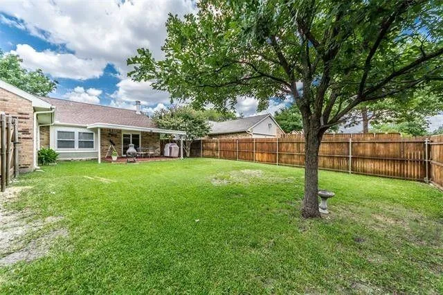 a view of house in front of a big yard with large trees and wooden fence